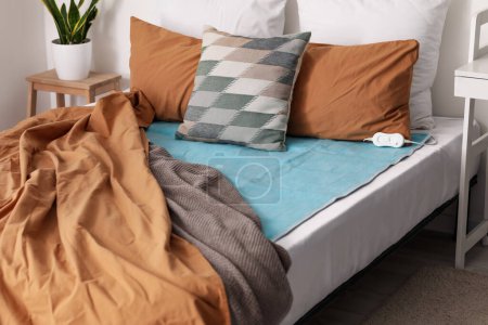 Cama con almohadas y almohadilla eléctrica en el dormitorio