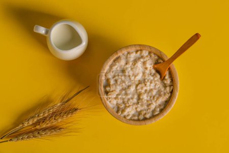 Photo for Bowl with oatmeal, spoon, wheat ears and pitcher on yellow background - Royalty Free Image