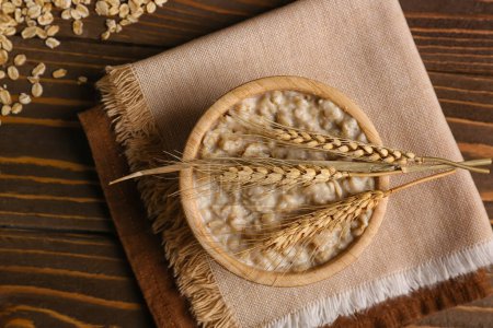 Photo for Bowl with tasty oatmeal, wheat ears and napkin on wooden background - Royalty Free Image