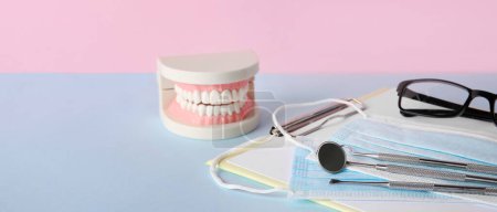 Foto de Mandíbula de plástico con herramientas dentales, portapapeles, máscaras médicas y anteojos en la mesa - Imagen libre de derechos