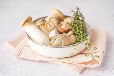 Bowl of fresh mushrooms and thyme on light background