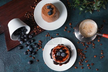Téléchargez les photos : Assiettes avec délicieux pudding au chocolat, tasse renversée de myrtille, grains de café et cappuccino en jezve sur la table - en image libre de droit