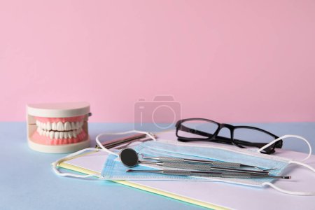 Foto de Modelo de mandíbula con herramientas dentales, portapapeles, máscaras y anteojos sobre mesa sobre fondo rosa - Imagen libre de derechos