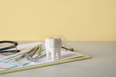 Foto de Diente de plástico con herramientas dentales, máscara y portapapeles sobre la mesa sobre fondo amarillo - Imagen libre de derechos