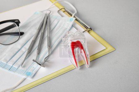Foto de Diente de plástico con herramientas dentales, máscara médica y portapapeles sobre fondo gris, primer plano - Imagen libre de derechos