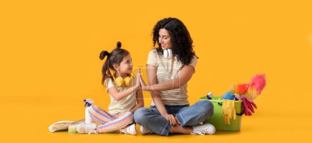 Foto de Mother and daughter with cleaning supplies giving each other high-five on yellow background - Imagen libre de derechos