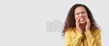 Téléchargez les photos : Young African-American woman suffering from tooth ache on light background with space for text - en image libre de droit