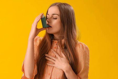 Sick young woman with inhaler on yellow background