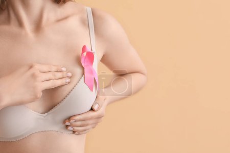 Téléchargez les photos : Young woman in underwear with pink ribbon on beige background. Breast cancer awareness concept - en image libre de droit