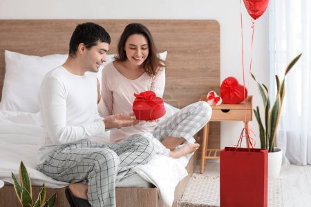 Foto de Young man receiving gift from his girlfriend in bedroom on Valentine's Day - Imagen libre de derechos