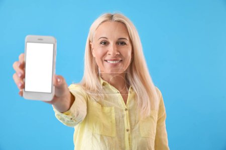 Foto de Mature blonde woman with mobile phone on blue background - Imagen libre de derechos