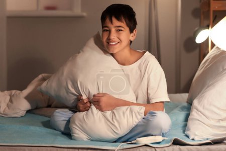 Photo for Little boy with pillow sitting on electric heating pad in bedroom at night - Royalty Free Image