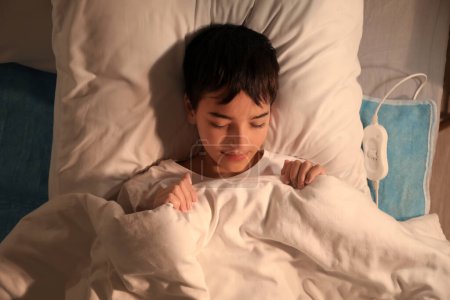 Photo for Little boy sleeping on electric heating pad in bedroom at night, top view - Royalty Free Image