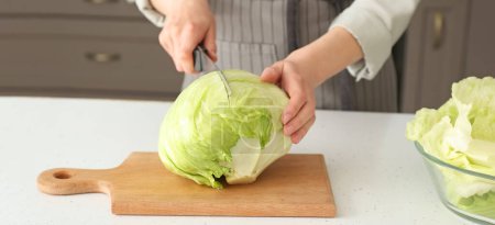 Woman cutting fresh iceberg lettuce on table in kitchen