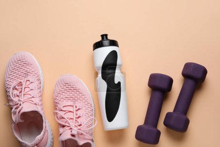 Sports water bottle with dumbbells and sneakers on beige background