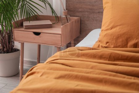 Téléchargez les photos : Wooden bedside table with books and reed diffuser in bedroom - en image libre de droit