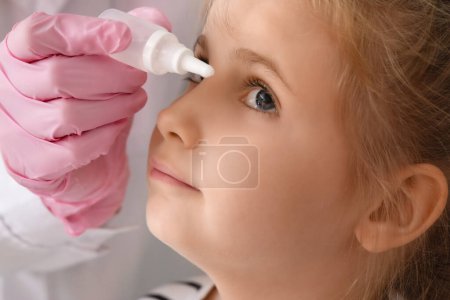 Foto de Ophthalmologist putting drops into little girl's eye in clinic, closeup - Imagen libre de derechos