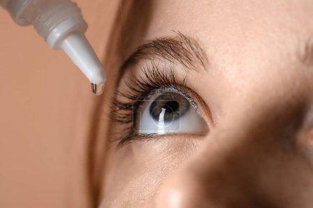 Foto de Young woman using eye drops on beige background, closeup - Imagen libre de derechos