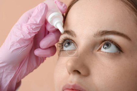 Foto de Ophthalmologist putting drops into young woman's eye on beige background, closeup - Imagen libre de derechos