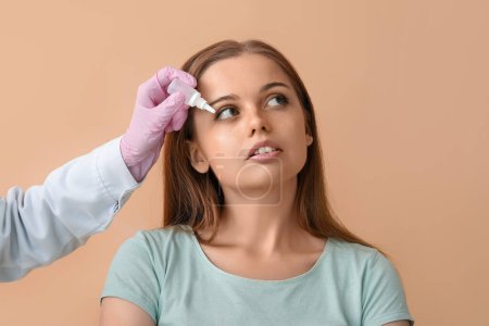 Foto de Ophthalmologist putting drops into young woman's eye on beige background - Imagen libre de derechos