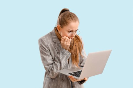 Photo for Young businesswoman with laptop biting nails on blue background - Royalty Free Image