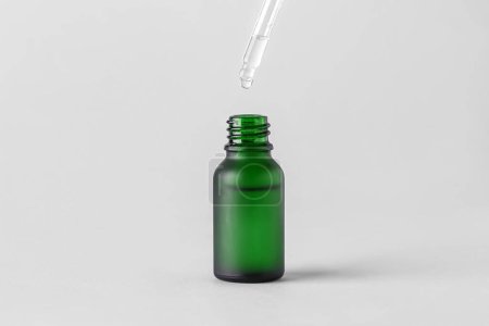 Téléchargez les photos : Dripping of serum into green glass bottle on light background - en image libre de droit