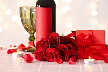 Téléchargez les photos : Bottle of wine, rose flowers, burning candles and glass on tile table against blurred lights. Valentine's Day celebration - en image libre de droit