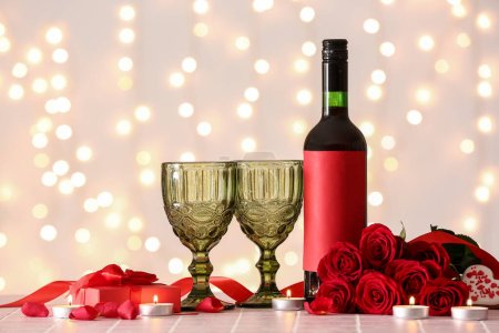 Téléchargez les photos : Bottle of wine, rose flowers, burning candles and glasses on tile table against blurred lights. Valentine's Day celebration - en image libre de droit