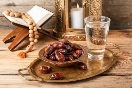 Tray with dried dates and glass of water for Ramadan on wooden table, closeup
