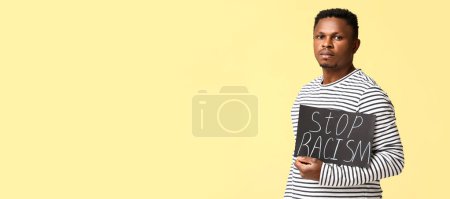 Photo for African-American man holding poster with text STOP RACISM on yellow background with space for text - Royalty Free Image