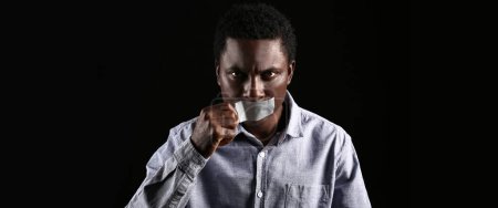 Téléchargez les photos : African-American man removing tape from mouth on dark background. Stop racism - en image libre de droit