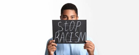 Foto de African-American teenage boy holding poster with text STOP RACISM on light background - Imagen libre de derechos
