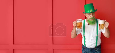 Foto de Mature man with green beard and mugs of beer on red background with space for text. St. Patrick's Day celebration - Imagen libre de derechos