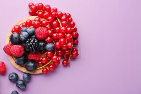 Wooden board with fresh ripe berries on color background