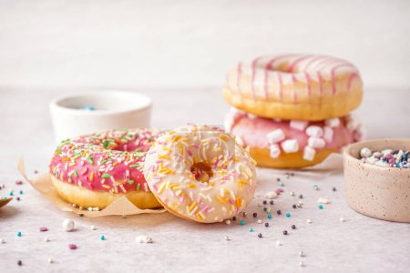 Photo for Parchments with different delicious donuts and bowls of sprinkles on white table - Royalty Free Image