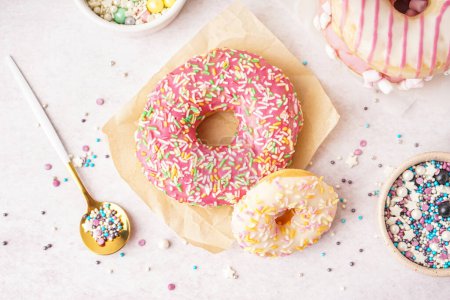 Téléchargez les photos : Parchments with different delicious donuts and bowls of sprinkles on white table - en image libre de droit