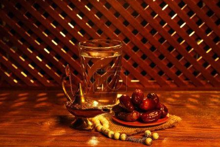 Aladdin lamp of wishes, prayer beads, glass and dates for Ramadan on wooden table