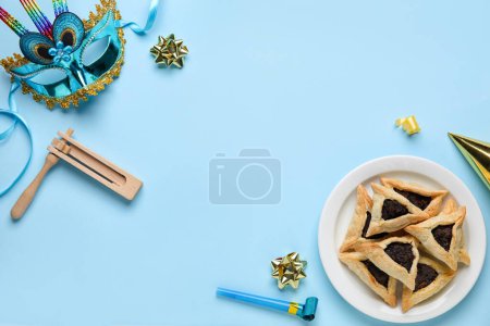 Foto de Frame made of Hamantaschen cookies, carnival mask and rattle for Purim holiday on blue background - Imagen libre de derechos