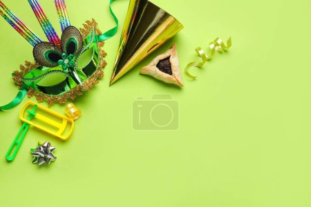 Foto de Hamantaschen cookie, carnival mask, party hat and rattle for Purim holiday on green background - Imagen libre de derechos
