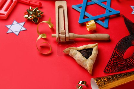 Téléchargez les photos : Hamantaschen cookie, carnival mask and rattles for Purim holiday on red background, closeup - en image libre de droit