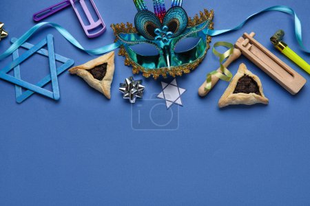Foto de Hamantaschen cookies, carnival mask and rattles for Purim holiday on blue background - Imagen libre de derechos