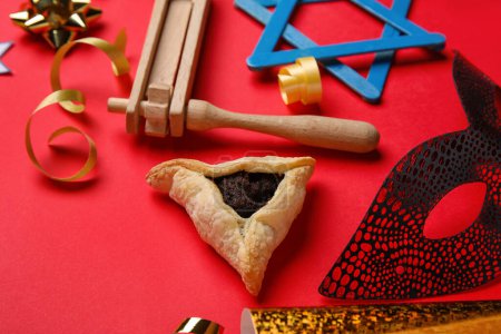 Téléchargez les photos : Hamantaschen cookie, carnival mask and rattle for Purim holiday on red background, closeup - en image libre de droit