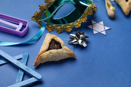 Téléchargez les photos : Hamantaschen cookie, carnival mask and rattle for Purim holiday on blue background, closeup - en image libre de droit