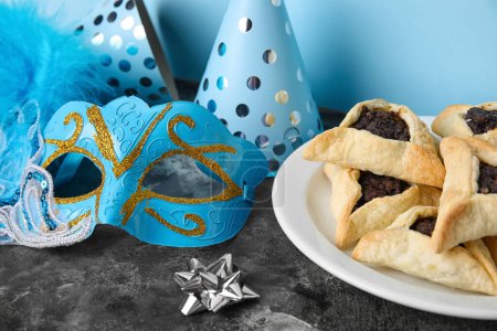 Foto de Hamantaschen cookies, carnival mask and party hats for Purim holiday on table near blue wall - Imagen libre de derechos