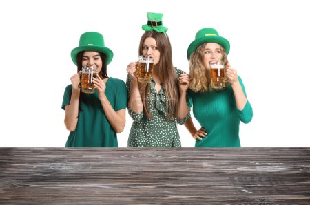 Foto de Beautiful young women with beer near table on white background. St. Patrick's Day celebration - Imagen libre de derechos