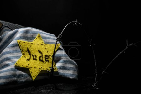Foto de Prisoner uniform, Jewish badge and barbed wire on black background with space for text. International Holocaust Remembrance Day - Imagen libre de derechos