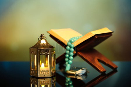 Téléchargez les photos : Lantern with glowing candle, Koran and prayer beads on table against blurred background. Islamic New Year celebration - en image libre de droit