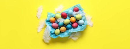 Téléchargez les photos : Œufs de Pâques colorés et plumes sur fond jaune - en image libre de droit