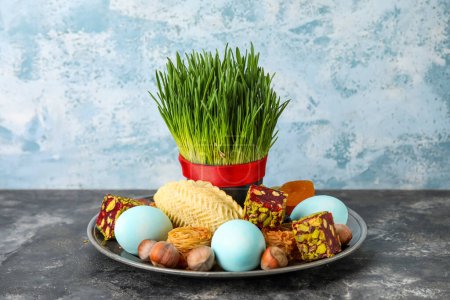 Plate with grass, eggs and treats on table near grunge wall. Novruz Bayram celebration