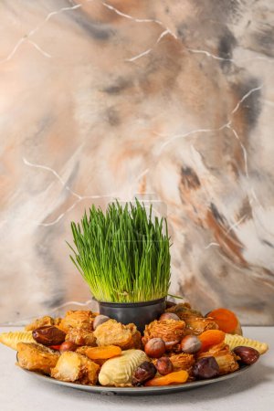 Foto de Plate with treats and grass on table near grunge wall. Novruz Bayram celebration - Imagen libre de derechos